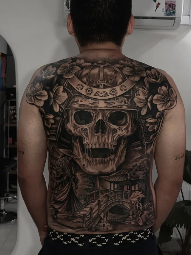 Full back black and grey Japanese tattoo of a samurai skull in a kabuto helmet with cherry blossoms, a ronin and a temple bridge