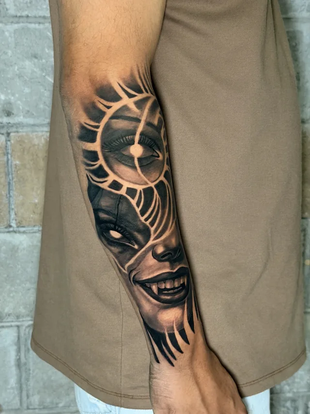 Black and grey realism inner forearm tattoo of a smiling vampire face with fangs merged into a radiant sun and eye