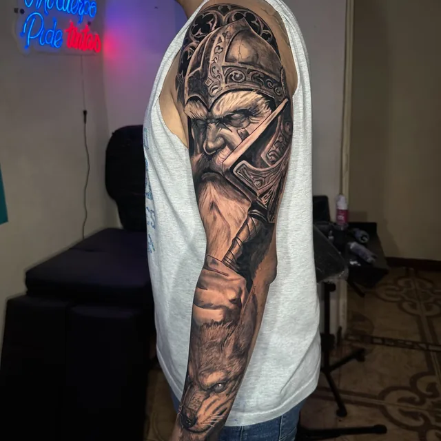 Black and grey realism arm sleeve tattoo of an armored bearded Viking warrior raising an axe above a wolf