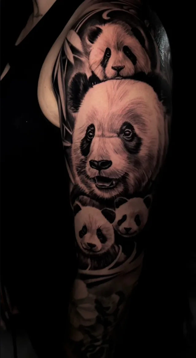 Black and grey realism upper arm tattoo of a giant panda portrait surrounded by panda cubs and bamboo