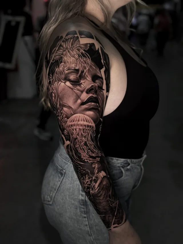 Black and grey realism full arm sleeve tattoo of a woman's face merging into an underwater scene with a jellyfish and sea turtle