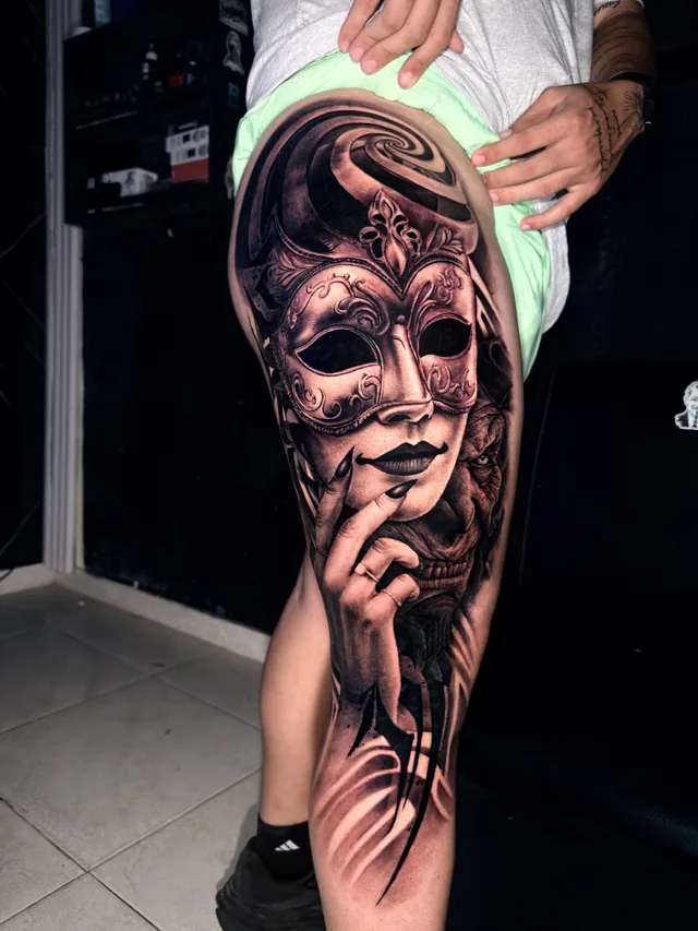Black and grey realism thigh and knee tattoo of a woman in an ornate Venetian masquerade mask beside a demonic figure