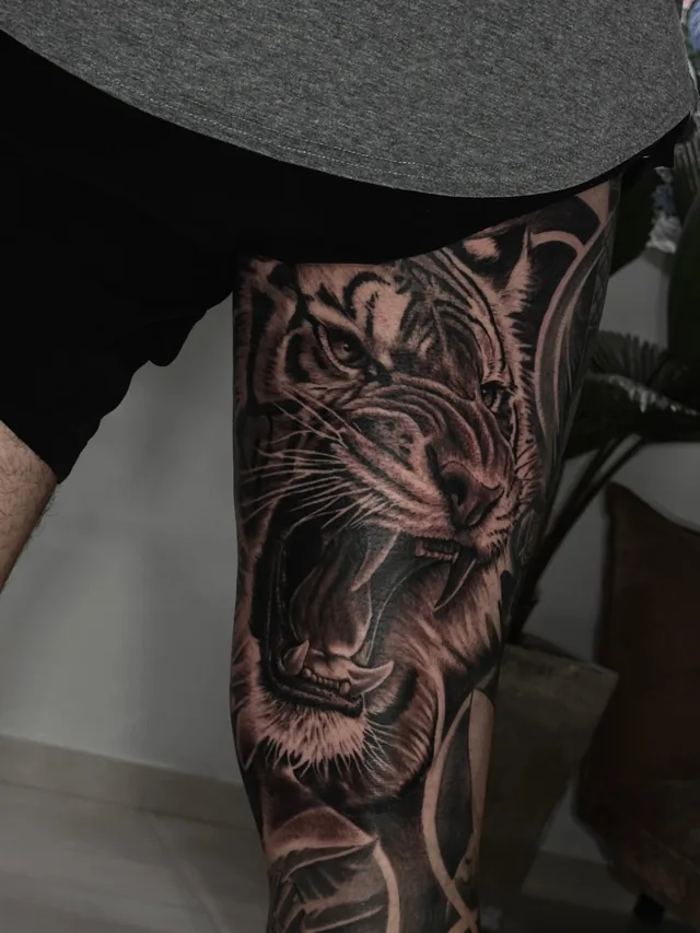 Black and grey realism thigh tattoo of a roaring tiger