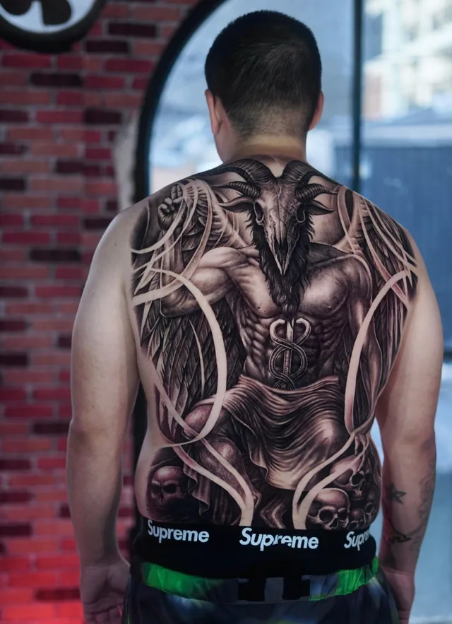 Full back black and grey tattoo of a winged Baphomet with a goat skull and serpents